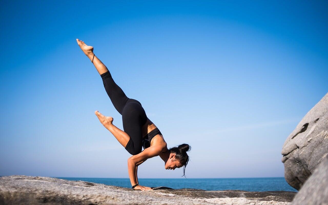 Woman balancing in a handstand on a rock by the ocean, symbolizing balance, energy, and thriving with Tech To Thrive personal coaching.
